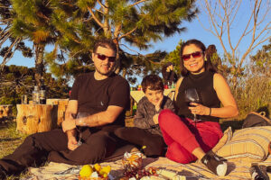 Caio, Carla e Ricardo sentados em uma toalha de pic-nic ao por do sol