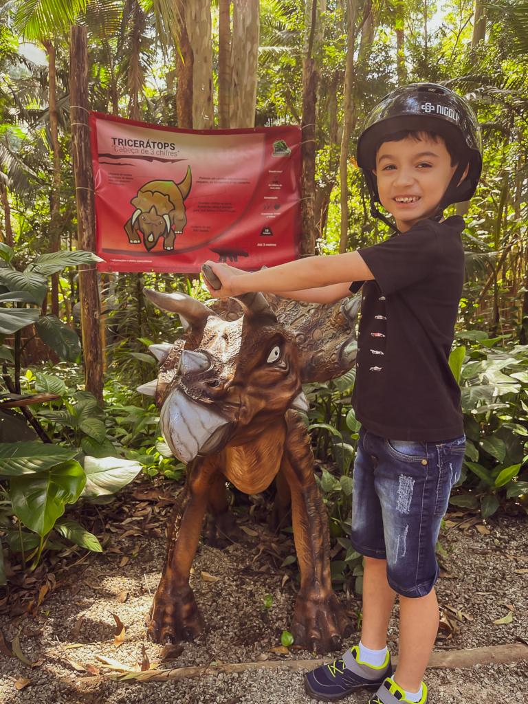 Caio na frente de um dinossauro filhote no Canto dos Dinossauros
